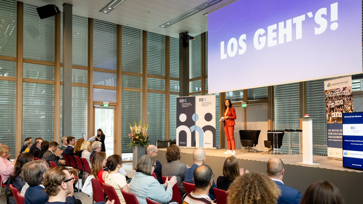 Start der Auftakt-Veranstaltung 2025 © Jörg Farys / BBE Auf einer Bühne steht eine Moderatorin. Hinter ihr steht auf einer Leinwand: "Los geht's!". Vor ihr sitzt Publikum.