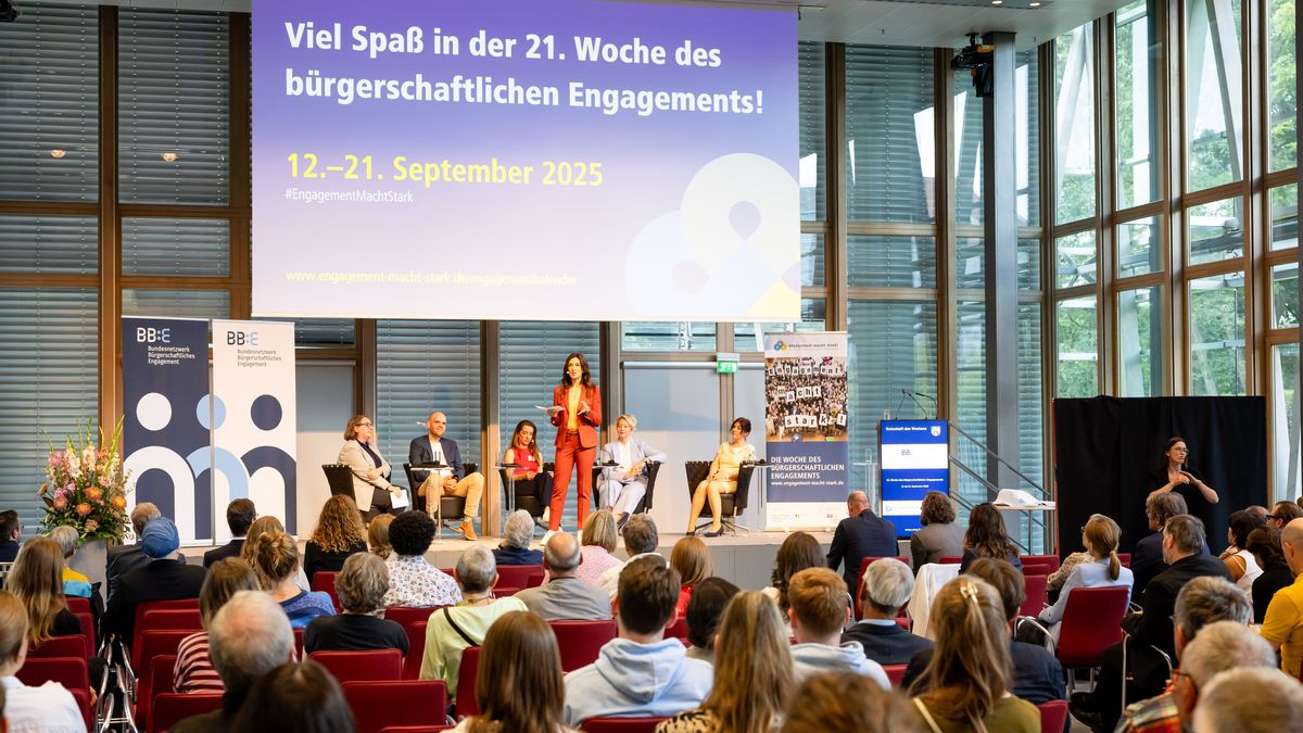 Ende des Auftakt-Programms 2025 © Jörg Farys / BBE Blick vom Publikum auf eine Bühne, auf der eine Frau steht und fünf Personen hinter ihr auf Sesseln sitzen. Darüber hängt eine Leinwand: "Viel Spaß in der 21. Woche des bürgerschaftlichen Engagements"