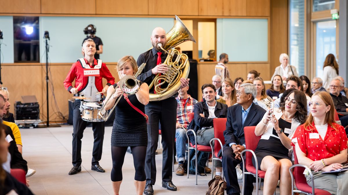 Walkabees © Jörg Farys / BBE Drei Personen mit Musikinstrumenten laufen durch einen Mittelgang an Publikum in einem Saal vorbei und musizieren.