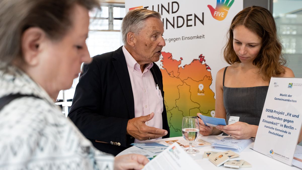 Iranische Gemeinschaft in Deutschland beim Markt der Gemeinsamkeiten © Jörg Farys / BBE Drei Menschen stehen an einem Stehtisch mit Infomaterialien und unterhalten sich.