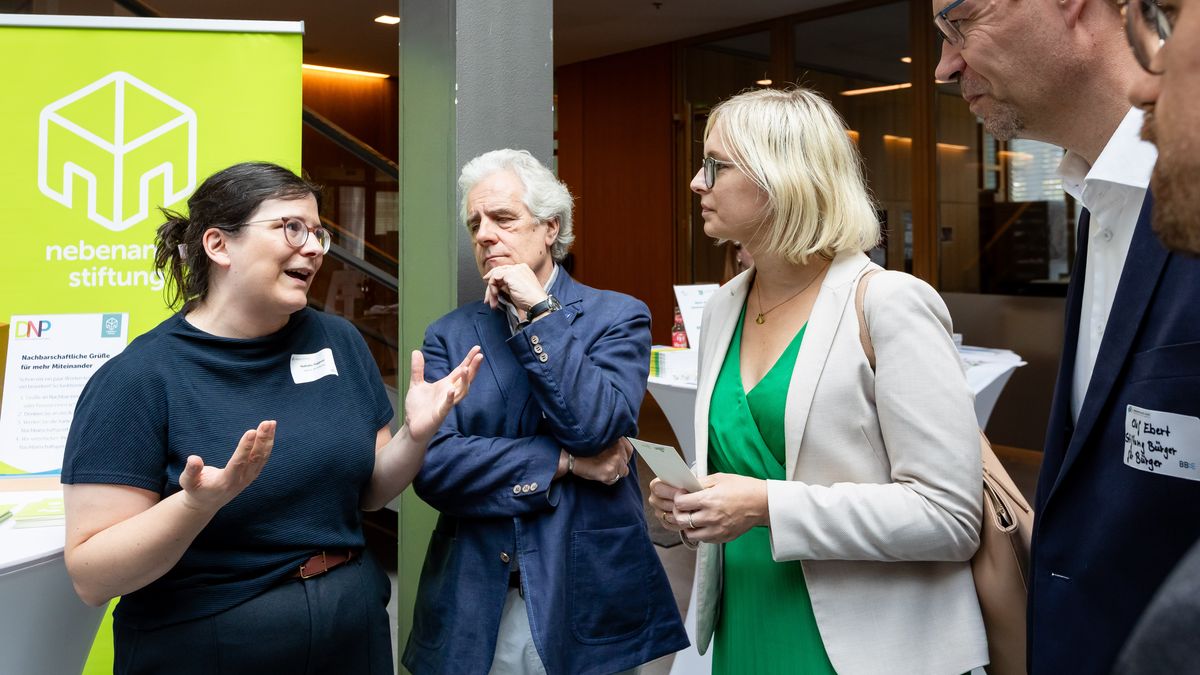 nebenan.de Stiftung auf dem Markt der Gemeinsamkeiten © Jörg Farys / BBE Staatsministerin Dr. Schenderlein spricht mit einer jungen Frau. Drei weitere Personen stehen dabei.