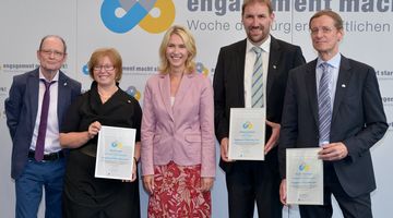 Die Engagement-Botschafter*innen 2014 Fünf Menschen stehen mit drei Urkunden vor einer Logowand.