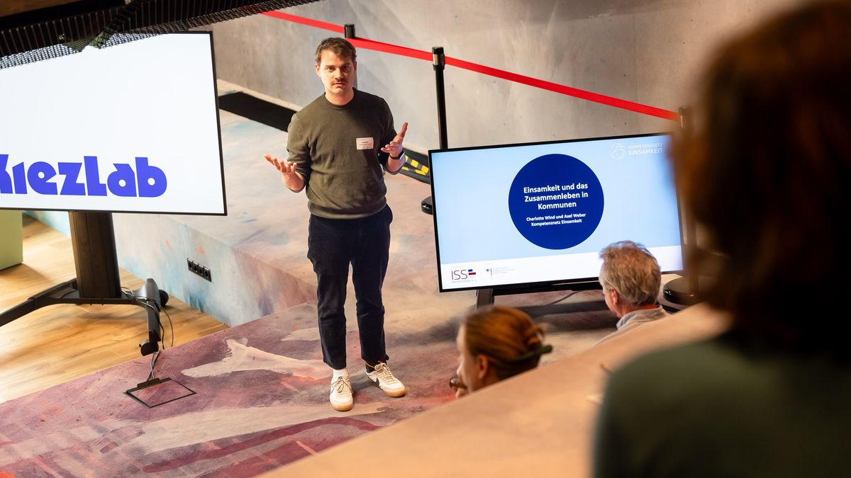 Workshop des Kompetenznetz Einsamkeit (KNE) © Jörg Farys Ein Mann steht auf einer kleinen Bühne vor sitzendem Publikum und spricht.