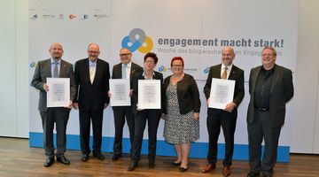 Engagement-Botschafter*innen 2015 Sieben Menschen stehen vor einer Logowand. Vier haben Urkunden in der Hand.