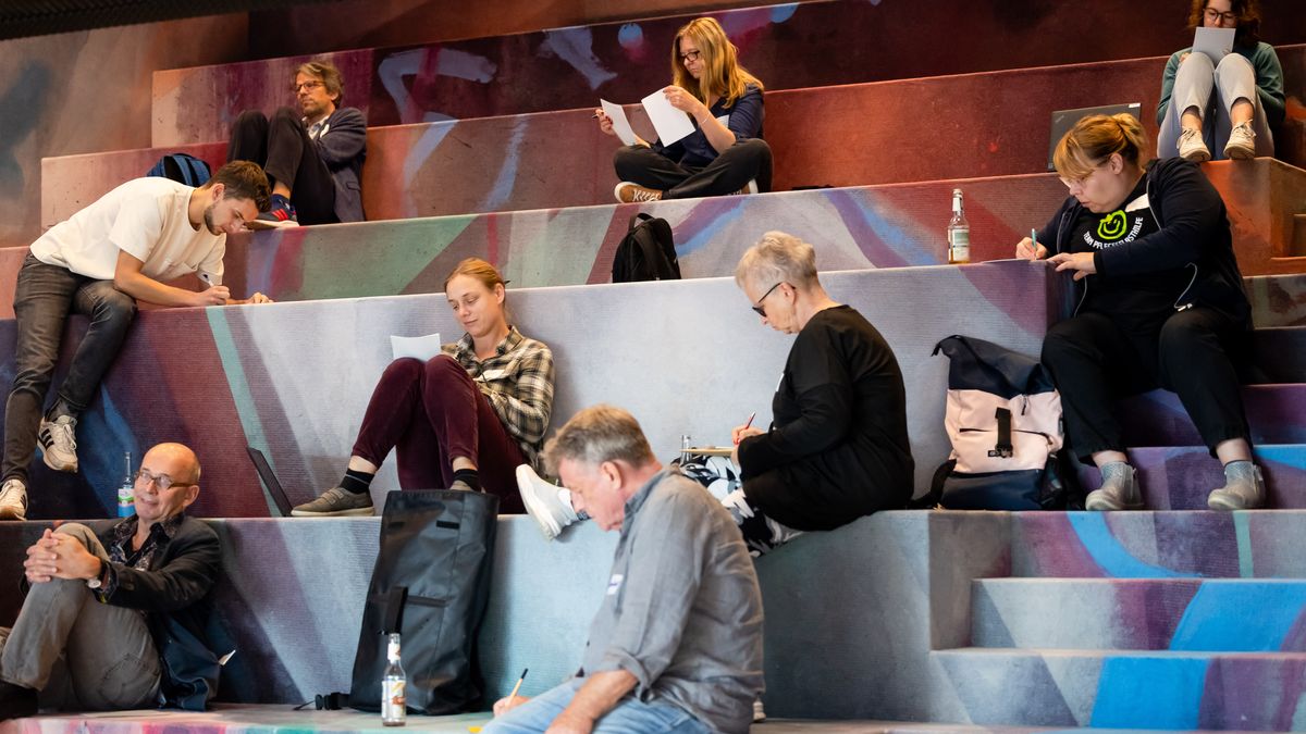 Workshopsituation © Jörg Farys In einem Raum mit treppenartigen Sitzgelegenheiten sitzen Personen und schreiben für sich auf Papier.